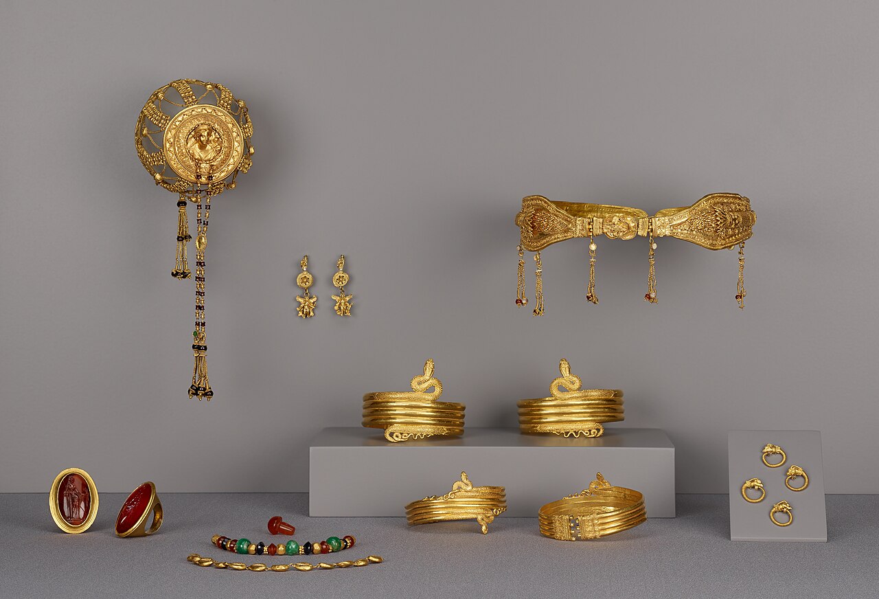 Colección de pulseras, anillos, aretes y otras joyas de oro sobre un fondo neutro